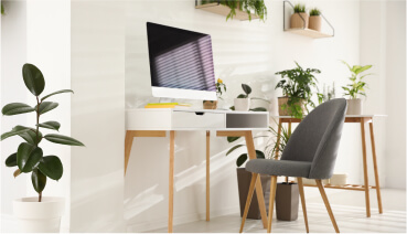 Interior of home office shows desk with computer surrounded by plants.